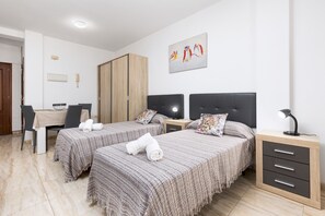 Hotellihuone, jossa on kaksi sänkyä, työpöytä, vaatekaappi, yöpöytä lampulla ja taulu seinällä.