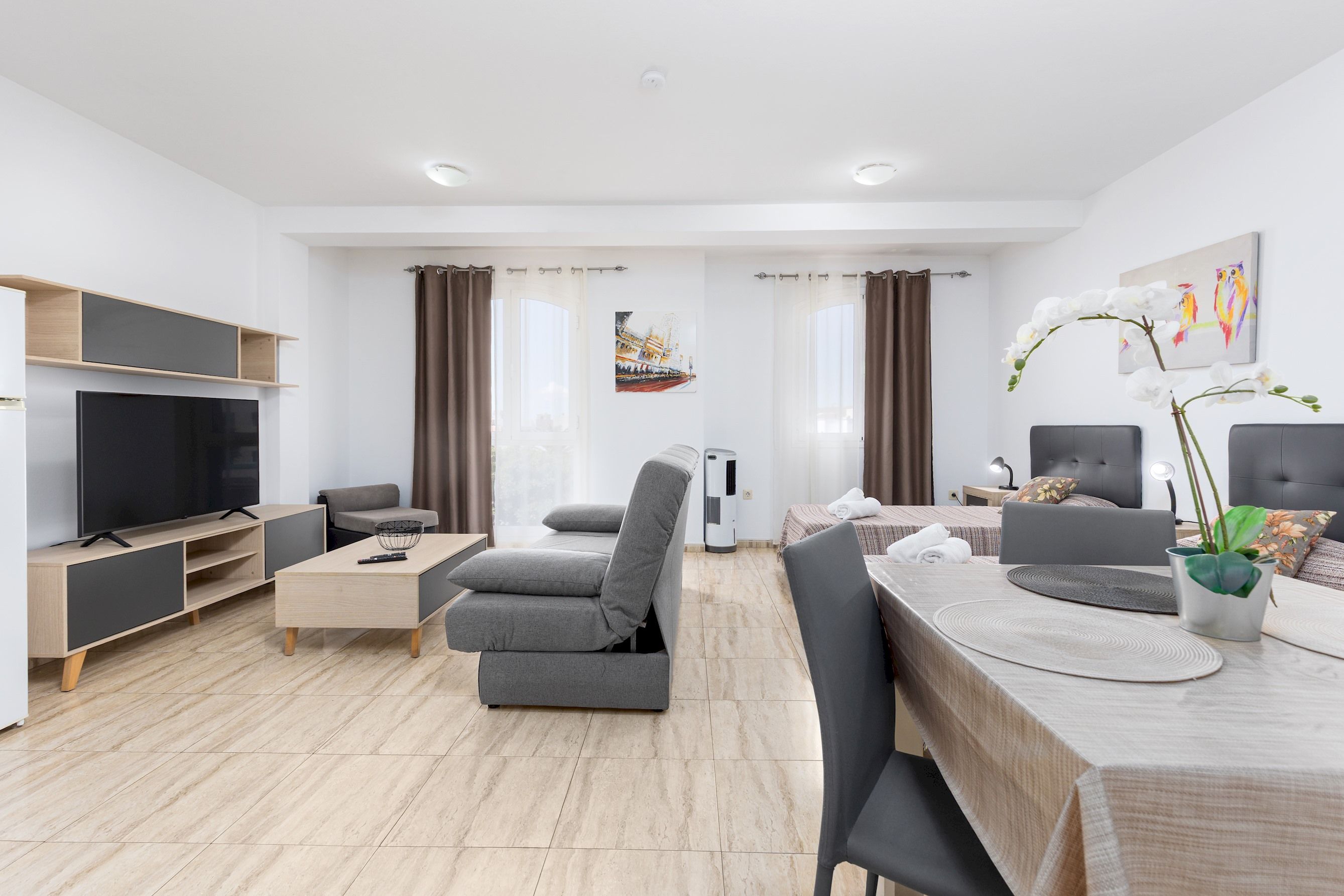 Una sala de estar moderna con un televisor de pantalla plana, un sofá, una mesa de comedor con sillas y una planta en maceta.