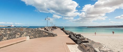 A wooden boardwalk leading to a sandy beach with a clear sky and a few clouds.