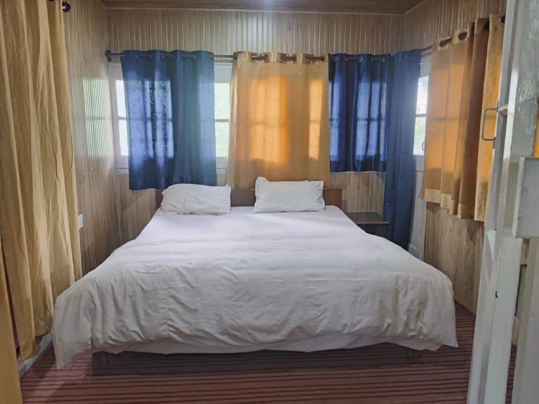 Uma cama de solteiro com roupa de cama branca num quarto com paredes de madeira e um tapete listrado.