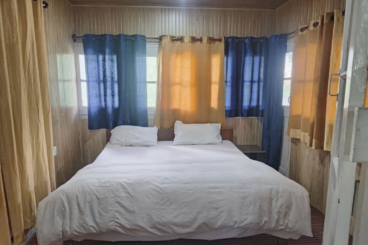 Uma cama de solteiro com roupa de cama branca num quarto com paredes de madeira e um tapete listrado.
