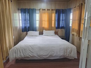 Uma cama de solteiro com roupa de cama branca num quarto com paredes de madeira e um tapete listrado.