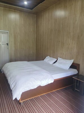 Un lit simple avec une literie blanche, dans une pièce aux murs lambrés et dotée d’un tapis à rayures.