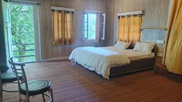 A bedroom with a bed, two windows with curtains, a chair, and a view of greenery outside.