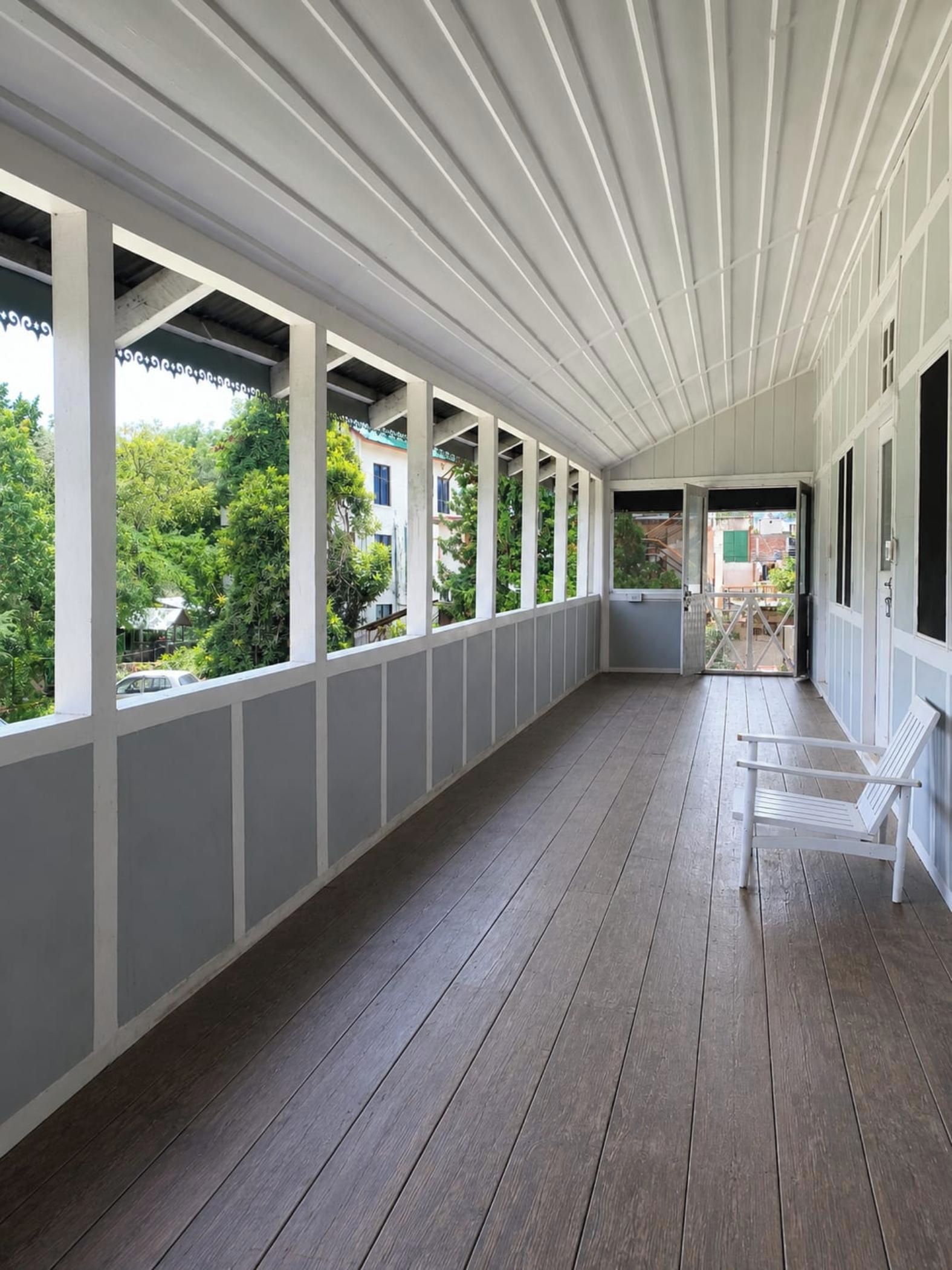 A covered porch with a wooden floor, white railings, and a bench.