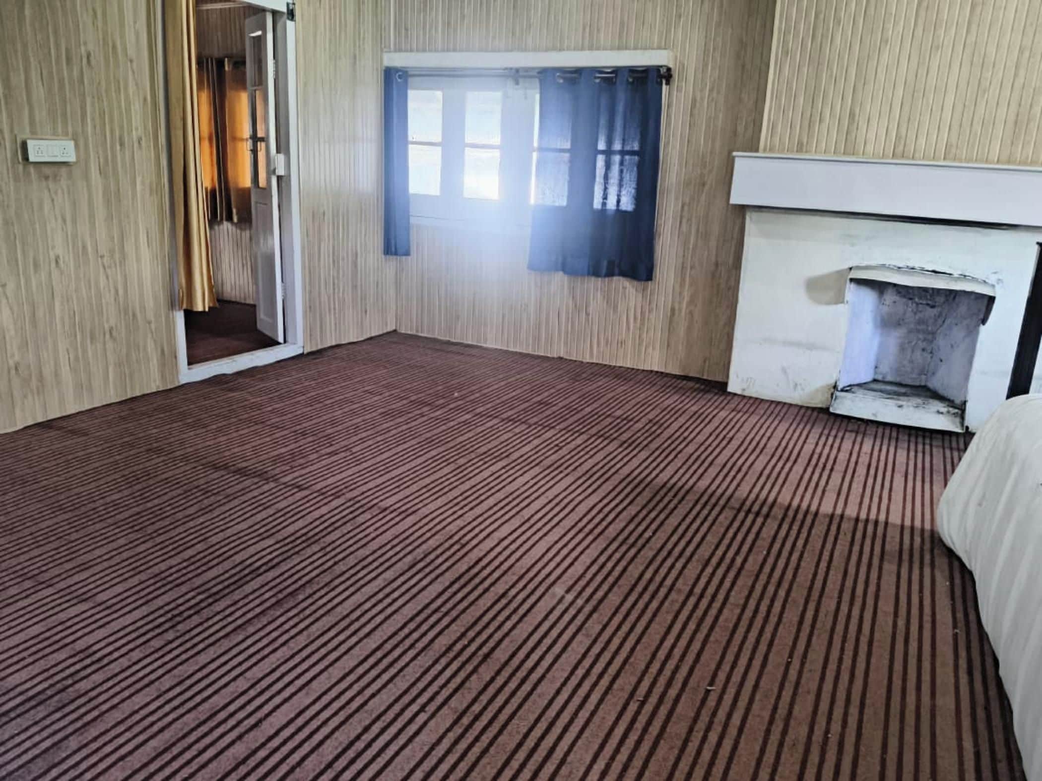 Una habitación con alfombra estampada, chimenea y ventana con cortinas.