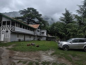 Un edificio de dos pisos con un balcón, un automóvil estacionado y una zona verde al frente.