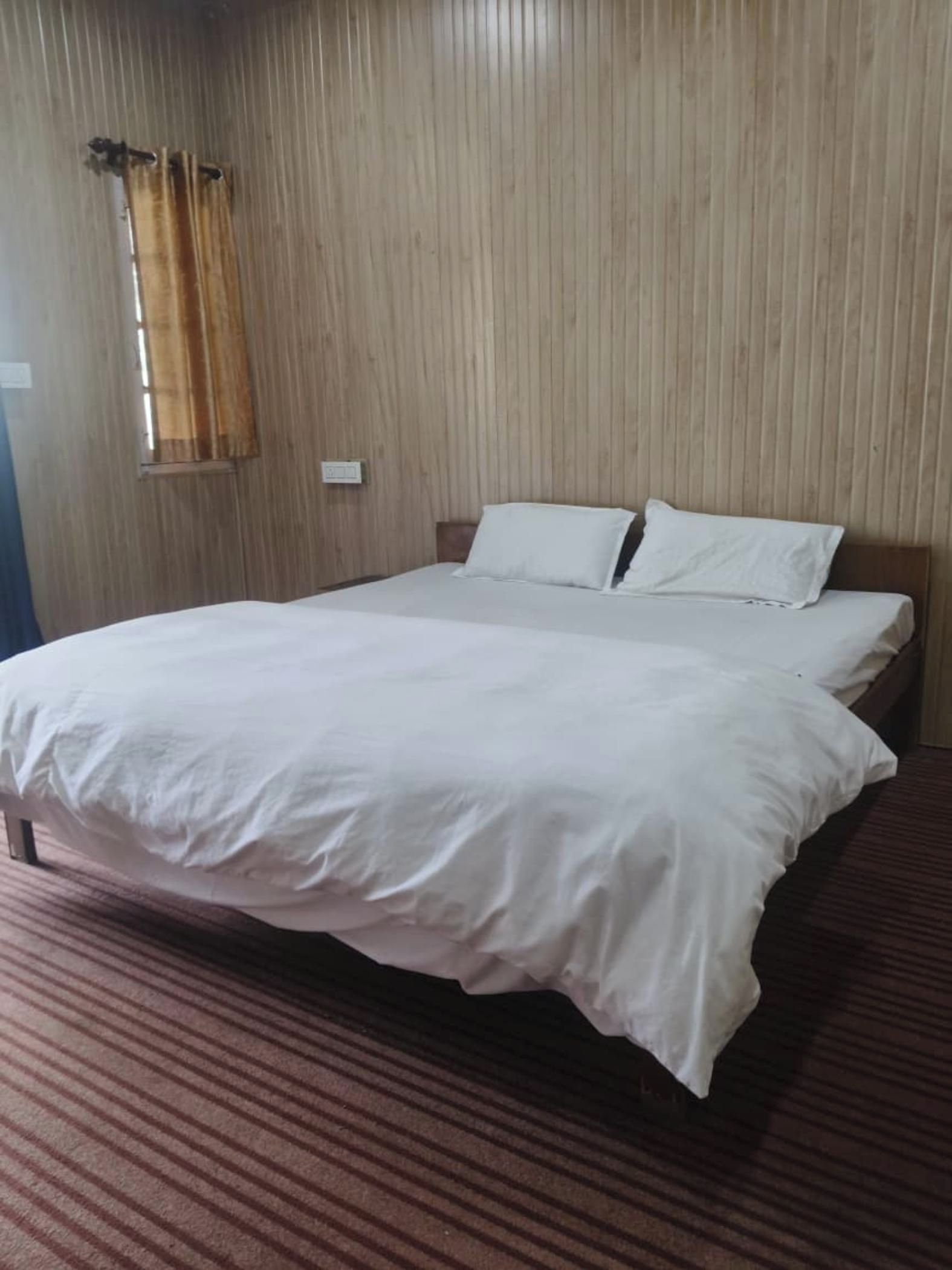 Una cama individual con ropa blanca en una habitación con paredes de madera y alfombra a rayas.