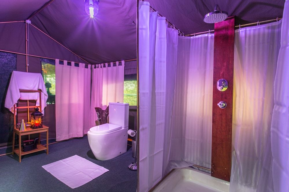 A tented room with a toilet, shower, and a small table with a lantern.