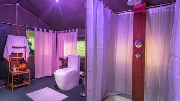 A tented room with a toilet, shower, and a small table with a lantern.