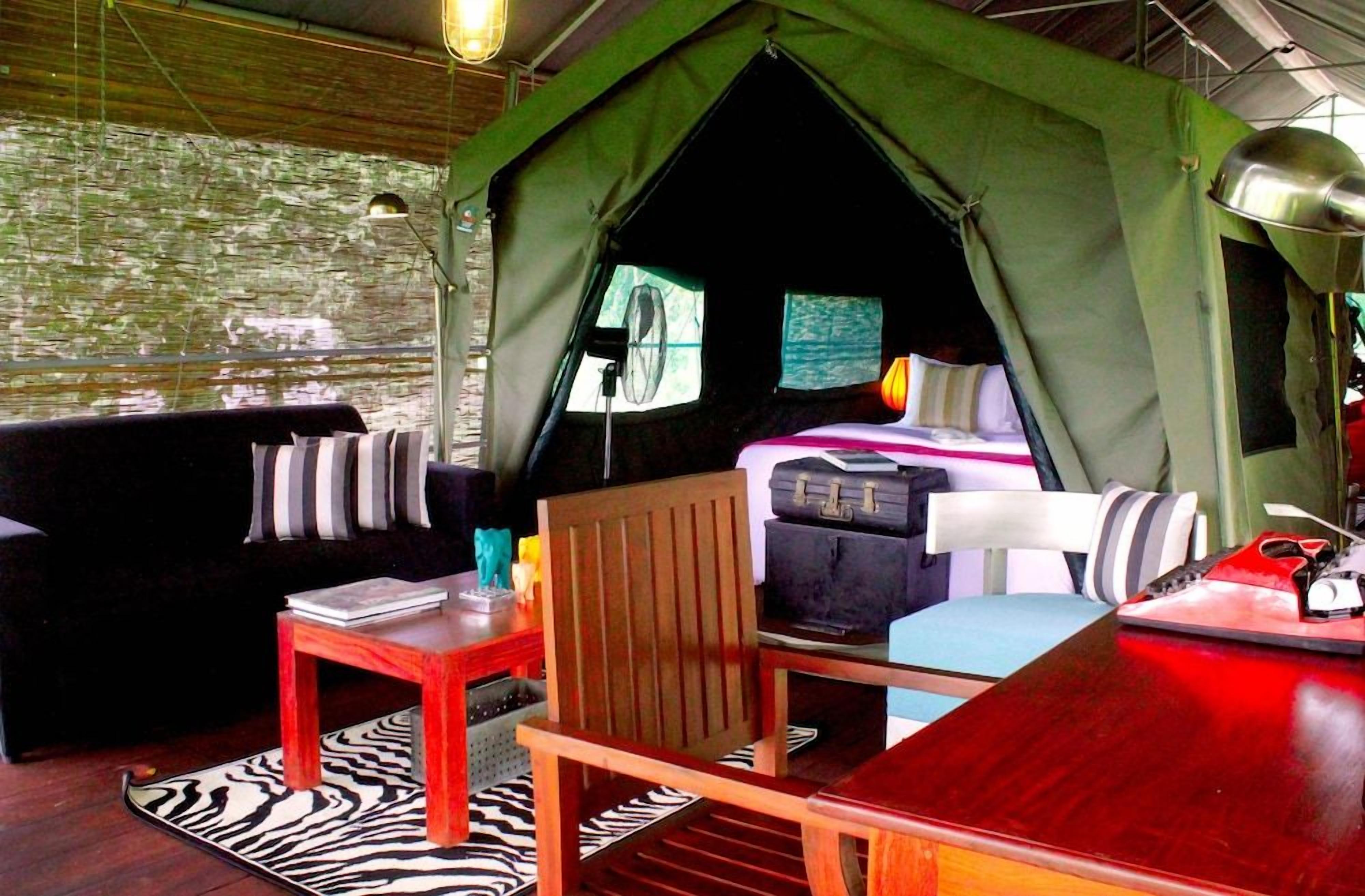 A tented accommodation with a bed, seating area, and a table.