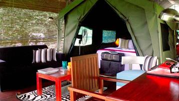 A tented accommodation with a bed, seating area, and a table.