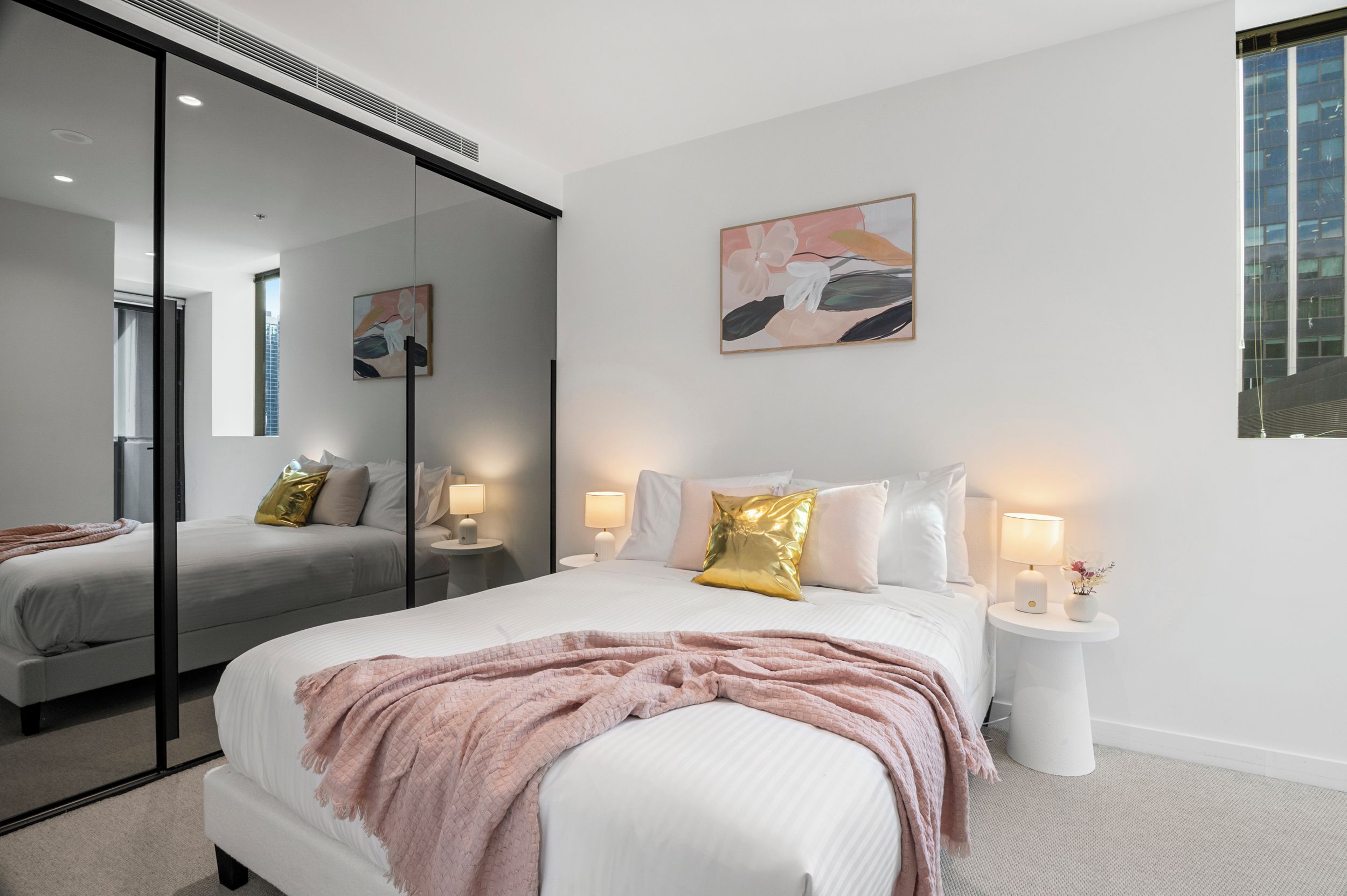 Un dormitorio moderno con una cama grande, lámparas de noche, un espejo y obras de arte en la pared.