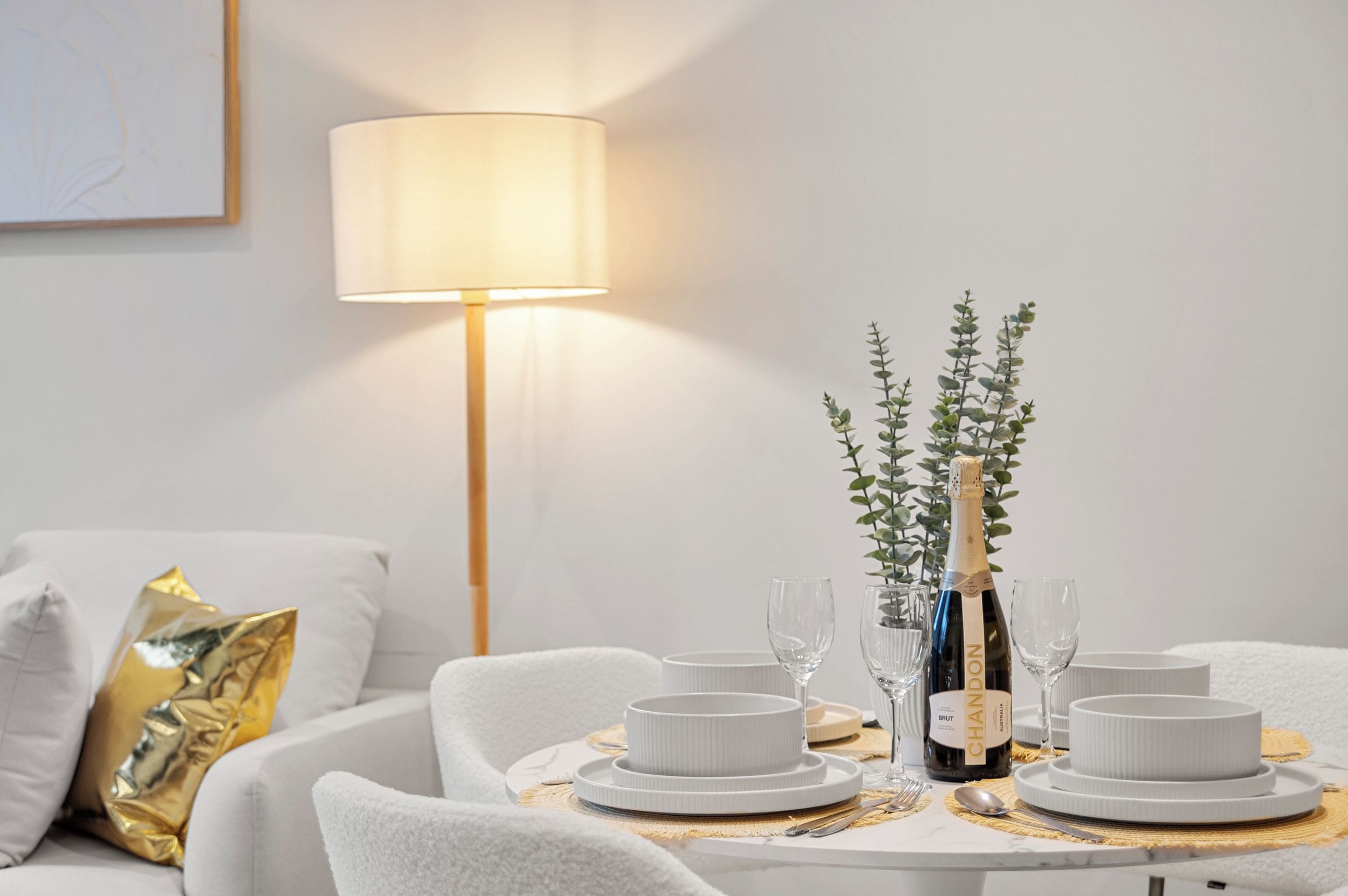 A dining table set with white plates, glasses, and a bottle of champagne.