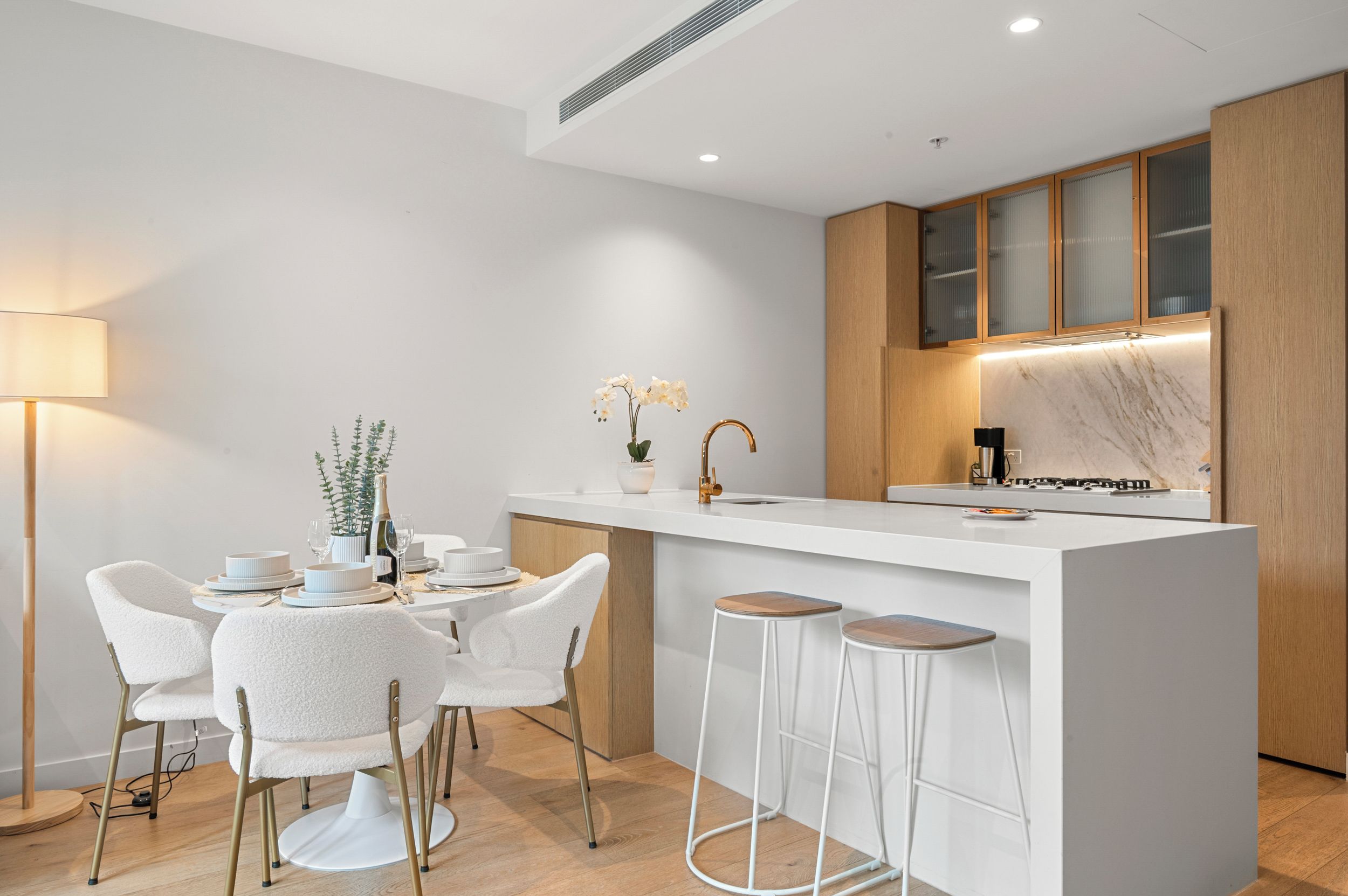 A modern kitchen with a white island, bar stools, and a dining area with white chairs.