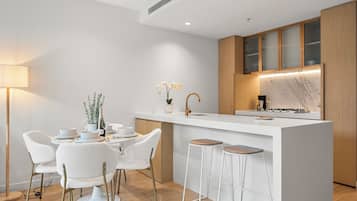 A modern kitchen with a white island, bar stools, and a dining area with white chairs.