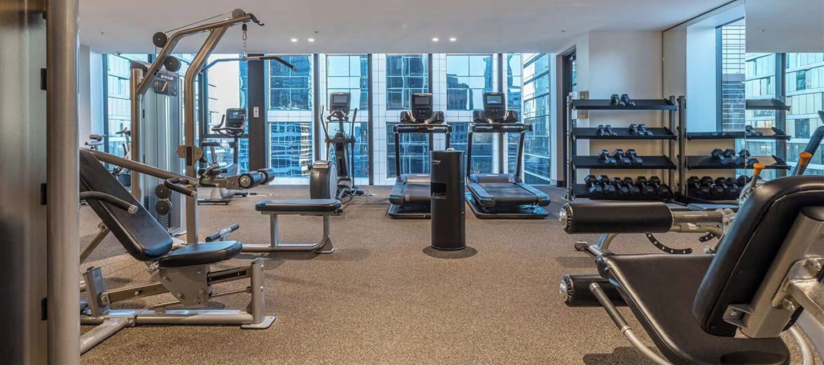 Un gimnasio moderno con equipo de ejercicio variado, ventanas amplias y vistas a la ciudad.