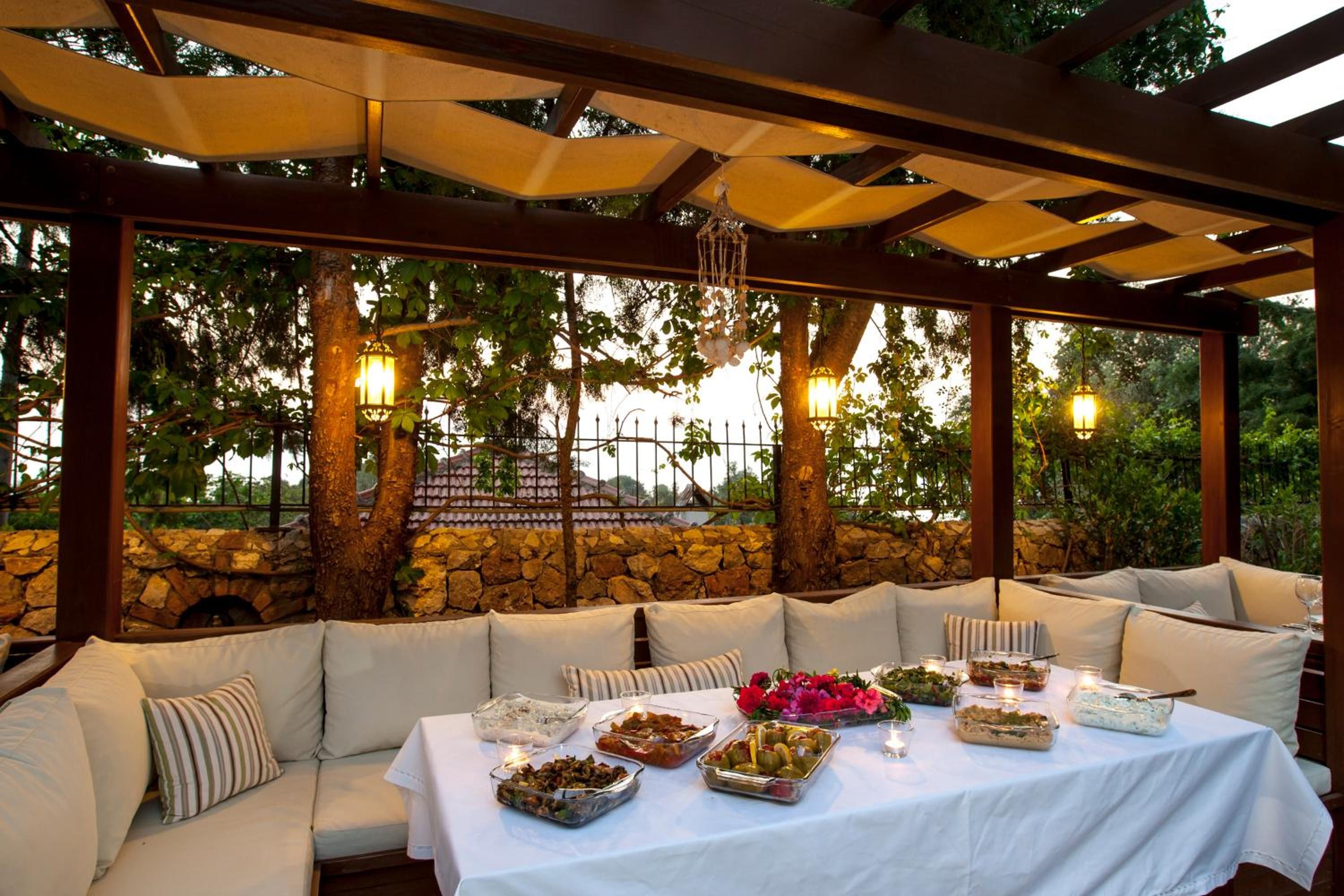 An outdoor dining area with a covered pergola, stone wall, and cushioned seating.
