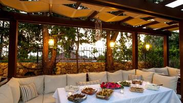 An outdoor dining area with a covered pergola, stone wall, and cushioned seating.