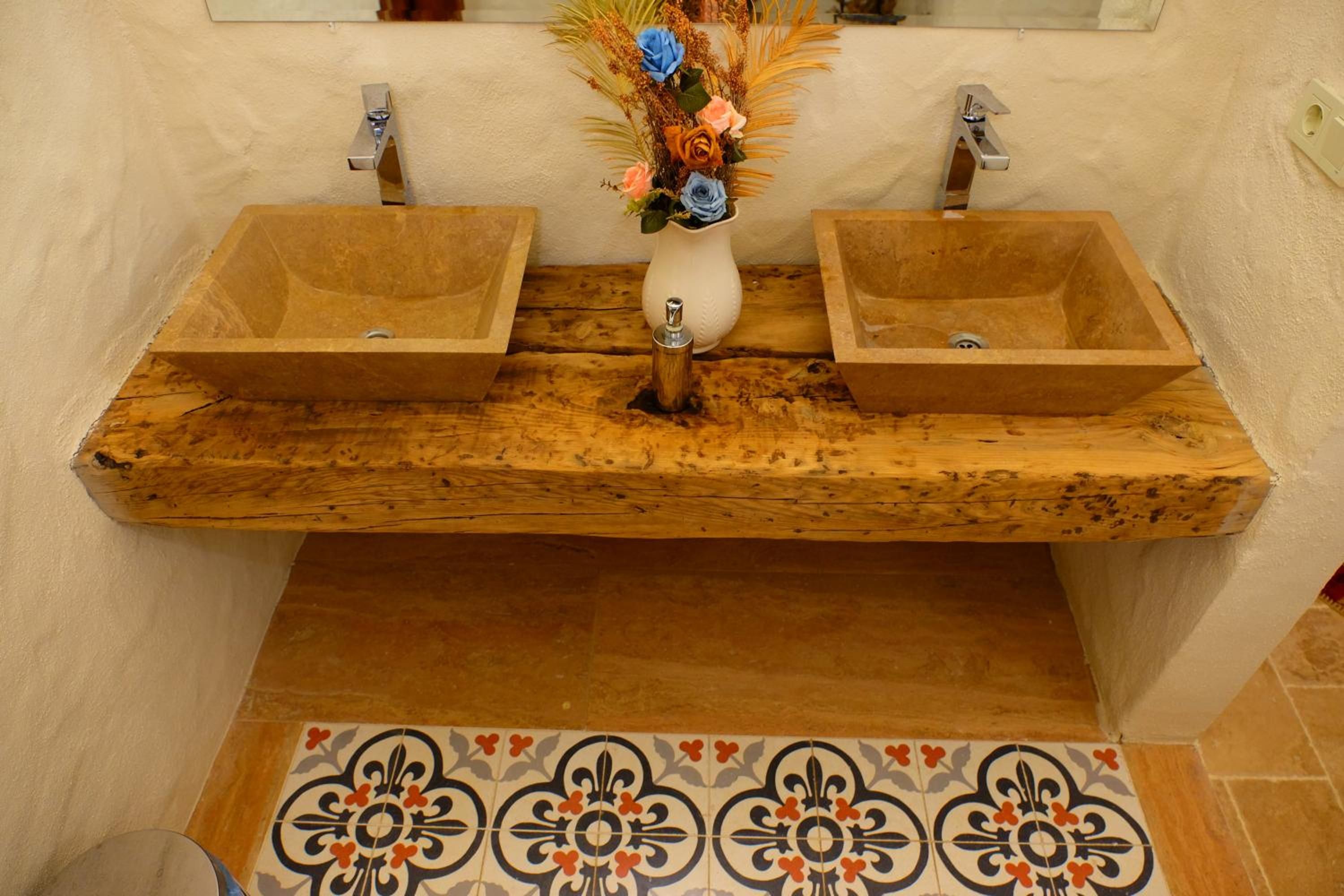 A bathroom with two wooden sinks, a white vase with flowers, and a patterned tile floor.