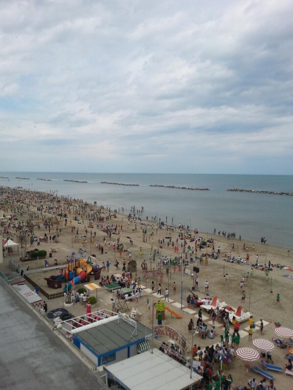 Praia cheia de gente, guarda-sóis e um parquinho.
