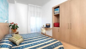 Quarto com cama, escrivaninha, armário e janela com cortinas.