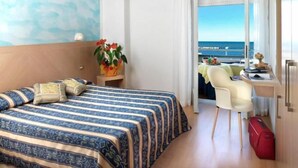 Hotellihuone, jossa on sänky, työpöytä, tuoli, matkalaukku ja näkymä merelle.