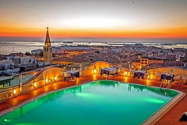A rooftop pool with a view of a cityscape and a sunset. - Hotel Astoria (Grado)
