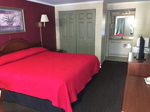 A hotel room with a large bed, a desk with a telephone, a mirror, and a wardrobe.