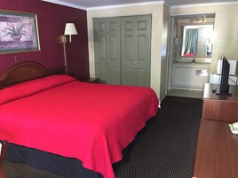 A hotel room with a large bed, a desk with a telephone, a mirror, and a wardrobe.