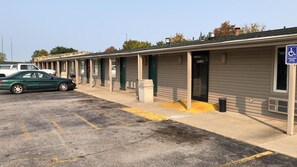 Fila de habitaciones de motel con un letrero de estacionamiento para discapacitados, un coche estacionado en el estacionamiento y un edificio con una puerta verde que dice 'OFICINA'.