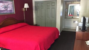 Una camera d'albergo con un letto grande, una scrivania con un computer, uno specchio e una porta che dà su un bagno.
