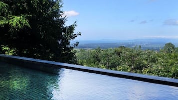Ein klarer Blick auf einen Pool mit einer gefliesten Kante, umgeben von üppiger Vegetation und einer entfernten Stadtlandschaft.