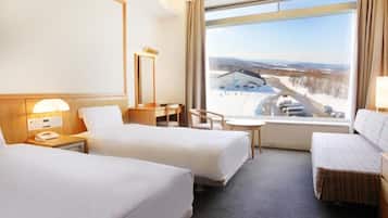 Ein Hotelzimmer mit zwei Betten, einem Schreibtisch, einem Stuhl und einem großen Fenster mit Blick auf eine verschneite Landschaft.