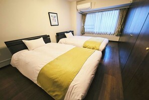 Habitación de hotel con dos camas, una ventana con cortinas, un equipo de aire acondicionado y un cuadro enmarcado en la pared.
