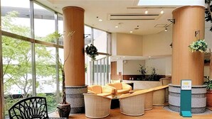 Un hall d’hôtel doté de grandes fenêtres, d’un comptoir d’accueil, de meubles en osier et de plantes en pot.