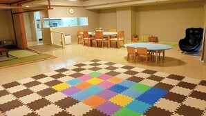 Une pièce spacieuse avec un grand tapis de sol coloré composé de pièces modulaires, une table à manger avec des chaises, et un coin cuisine à l’arrière-plan.