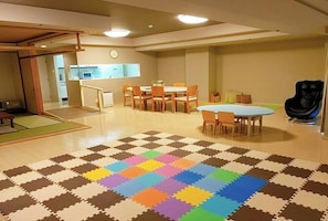 Una habitación amplia con un tapete grande y colorido de piezas entrelazadas, una mesa de comedor con sillas y una cocina al fondo.