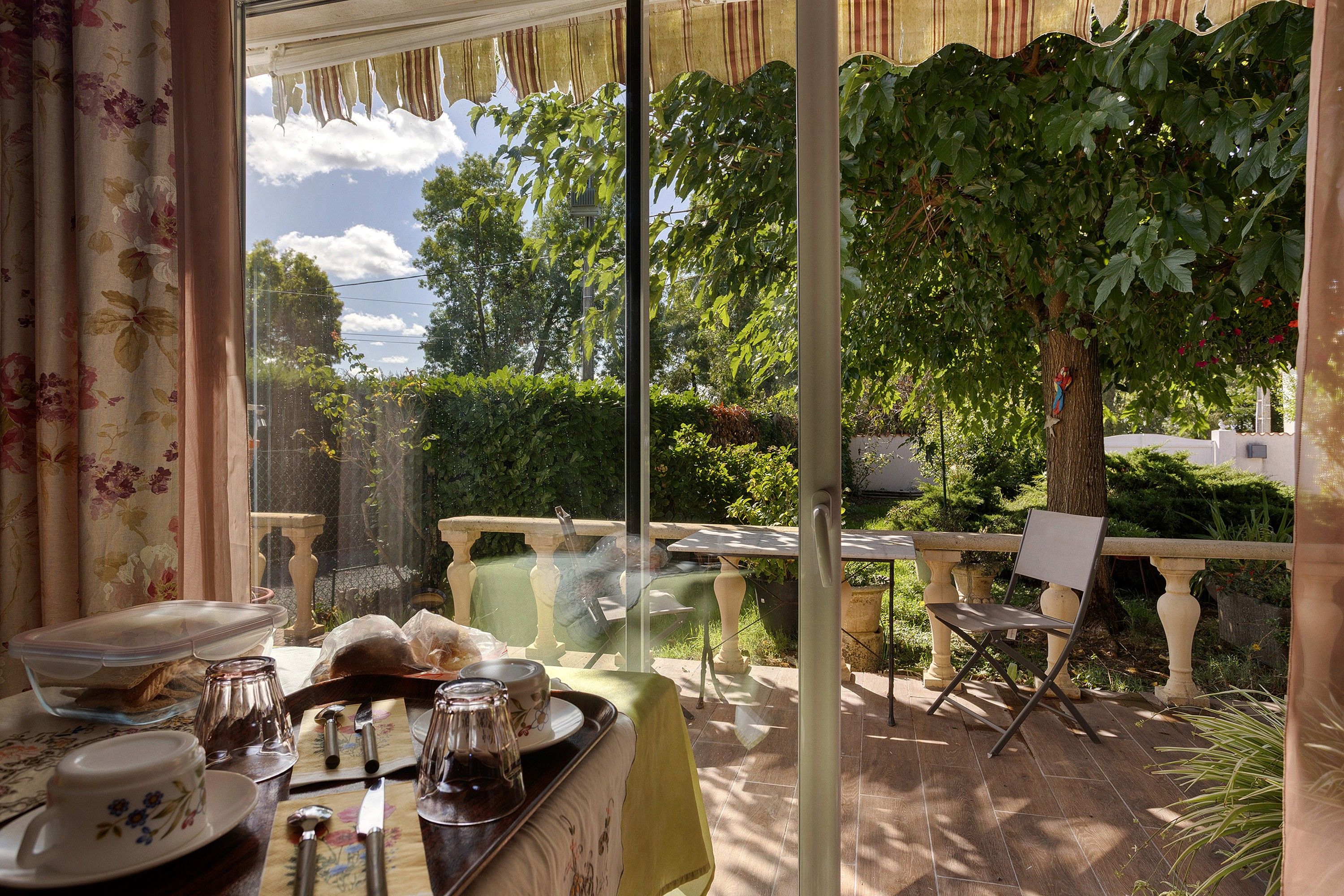 Un coin repas avec une table dressée pour deux personnes, une chaise et une vue sur un jardin, visible à travers une porte vitrée.