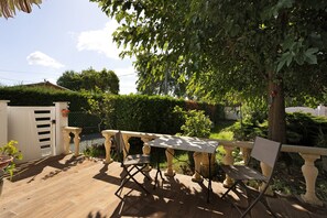 A patio with a table and chairs, surrounded by greenery and a white fence.