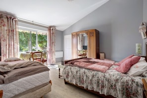 A bedroom with two beds, a wooden wardrobe, a table with chairs, and a window with curtains.