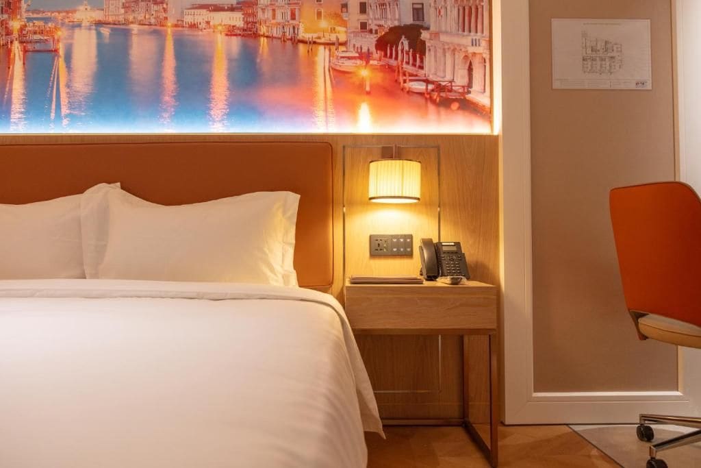 A hotel room with a bed, a nightstand with a lamp, a telephone, and a chair.