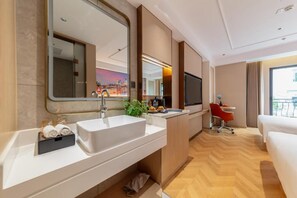 Una camera d'albergo con un grande specchio, un lavandino bianco, una piccola scrivania con una sedia e un letto.