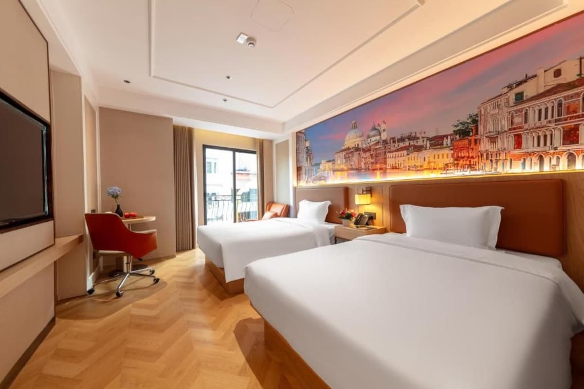 Una camera d'albergo con due letti, una scrivania, una sedia e un'ampia finestra.