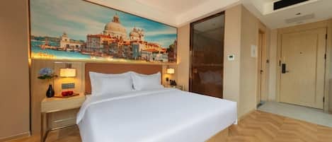 A hotel room with a bed, a nightstand, a lamp, a painting of a cityscape, and a door.