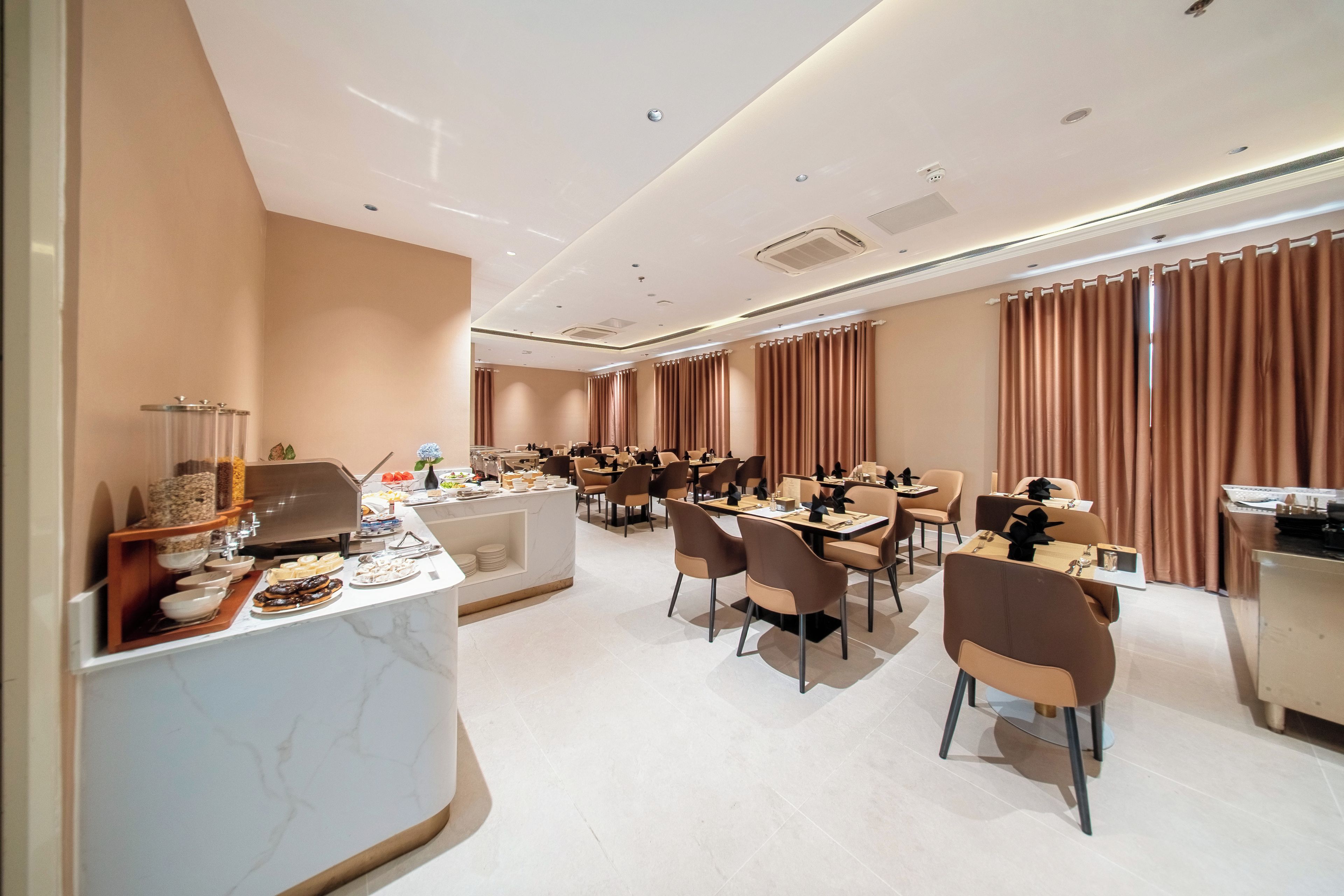 A hotel dining area with multiple tables and chairs, a buffet station, and a reception desk.