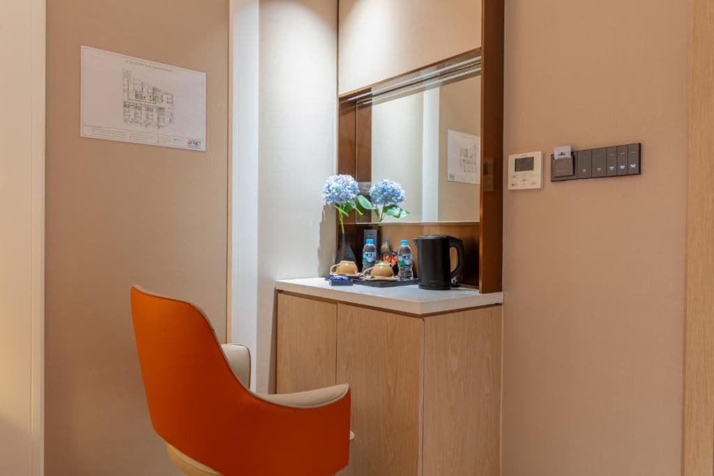 A hotel room with a wooden cabinet, a mirror, a coffee maker, and a chair.