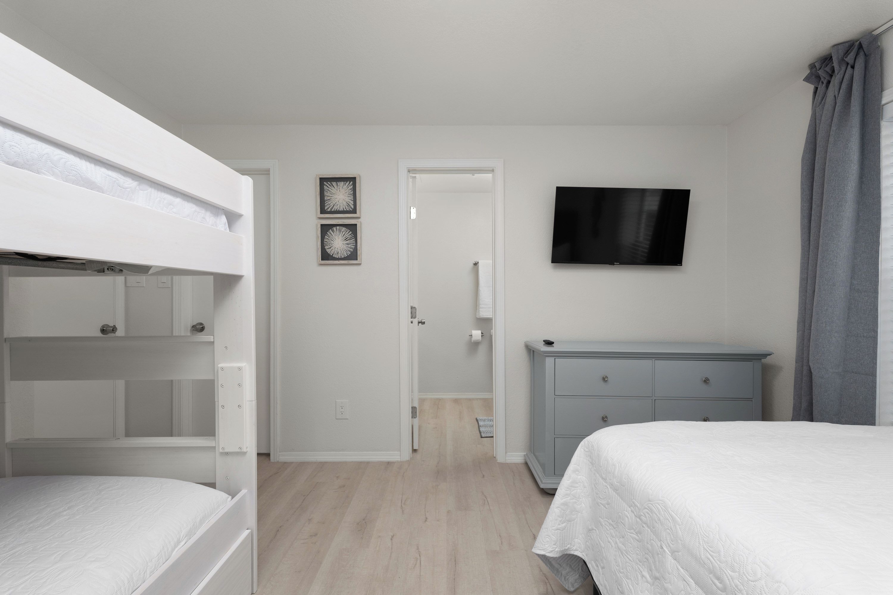 A bedroom with bunk beds, a dresser, a flat-screen TV, and a door leading to another room.