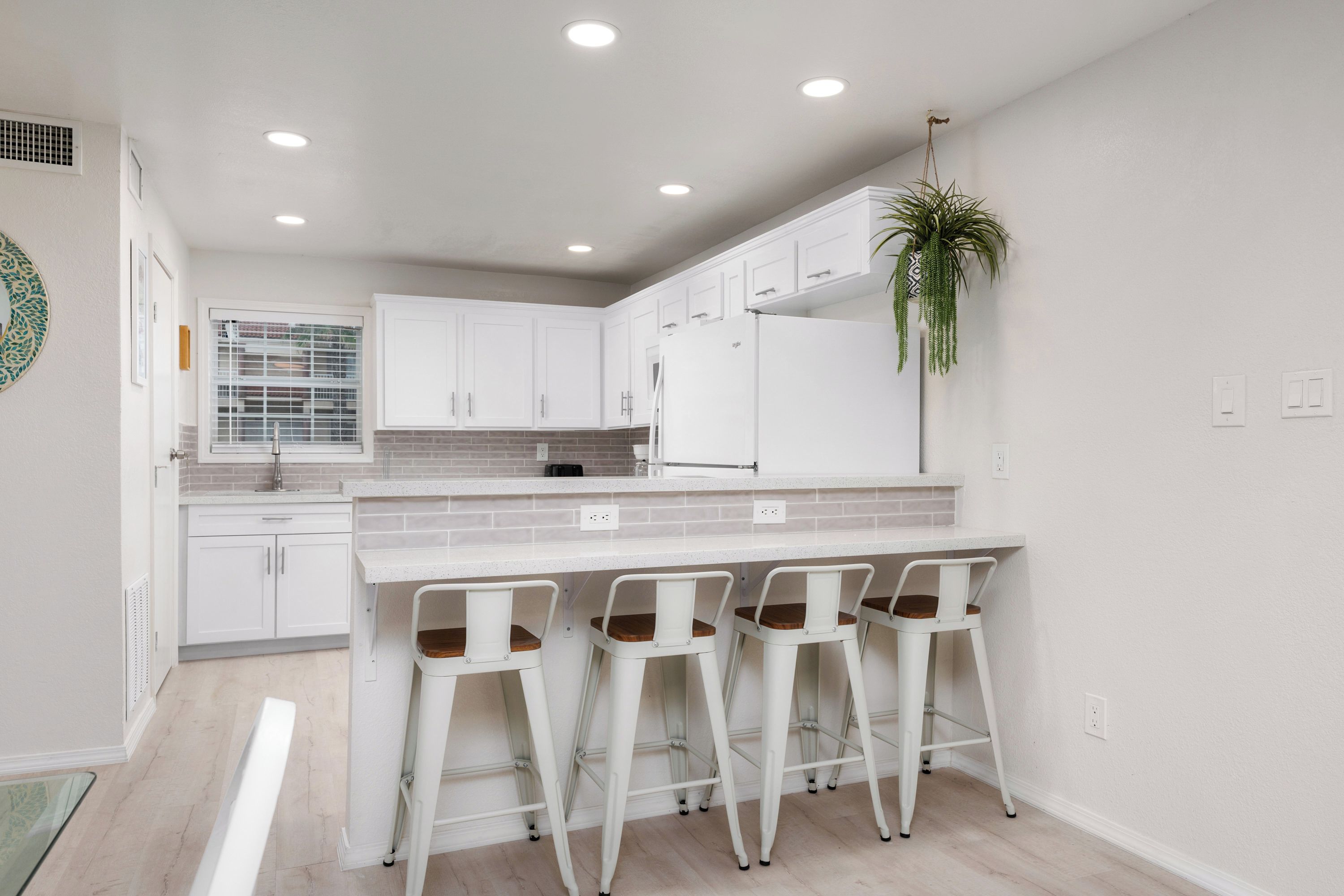 A modern kitchen with white cabinets, a marble countertop, and bar stools.