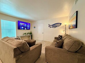 Un salon avec deux canapés, un téléviseur à écran plat, un décor mural représentant des poissons et un tableau.